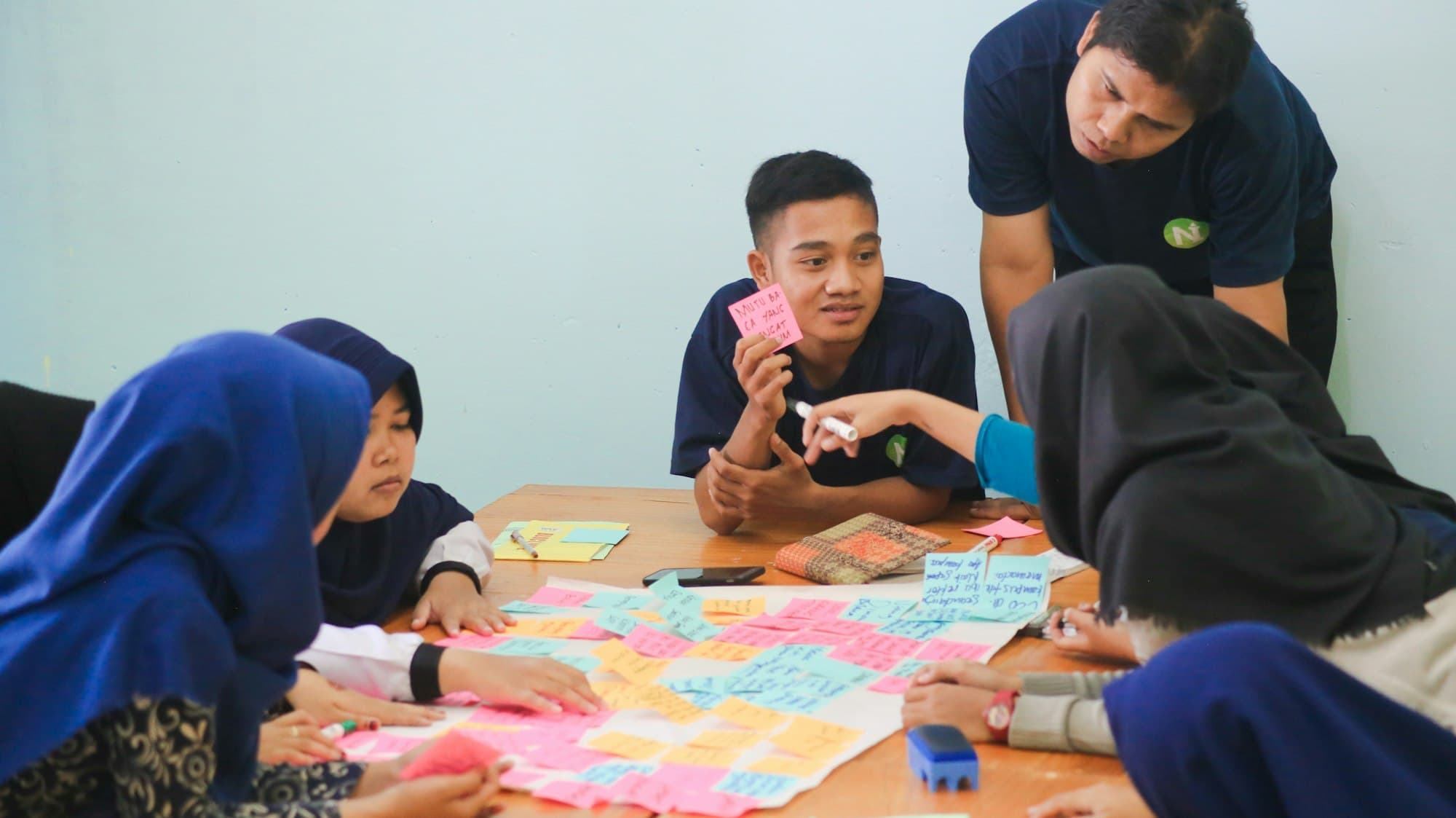 Students leaning over a table covered in sticky notes, planning together